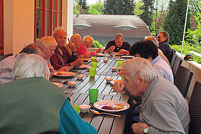 Etwa zwölf Tagesgäste essen gemeinsam an einem langen Tisch auf der Terrasse
