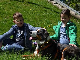 ein Mädchen und ein Junge sitzen auf der Wiese und streicheln einen größeren Hund